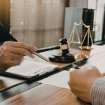 Advokat u kancelariji pokazuje dokument klijentu dok ovaj potpisuje ugovor za stolom