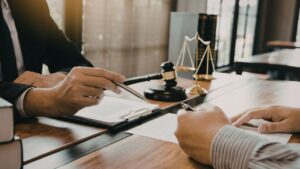 Advokat u kancelariji pokazuje dokument klijentu dok ovaj potpisuje ugovor za stolom