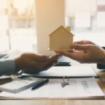 osobe potpisuju dokumentaciju za prenos vlasništva i predaju maketu kuće jedna drugoj