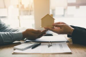 osobe potpisuju dokumentaciju za prenos vlasništva i predaju maketu kuće jedna drugoj