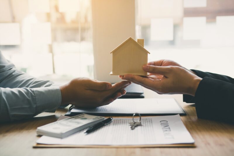 osobe potpisuju dokumentaciju za prenos vlasništva i predaju maketu kuće jedna drugoj